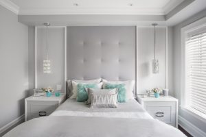 Horizontal image of modern girls bedroom, with large headboard and matching side tables and lamps. Brightly lit with pastel colours and pops of turquoise.